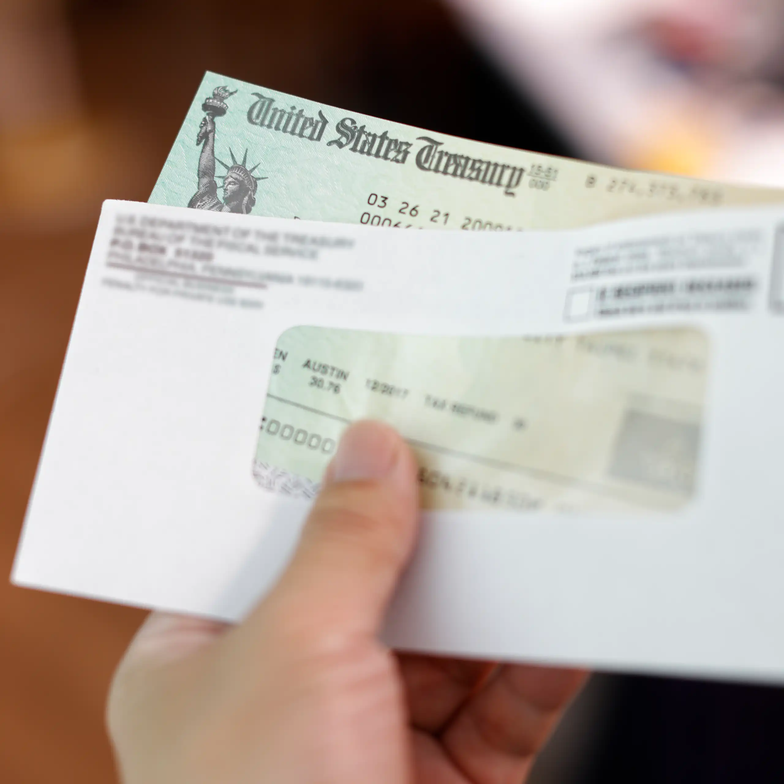 A hand holds an envelope with a check from the US treasury inside.