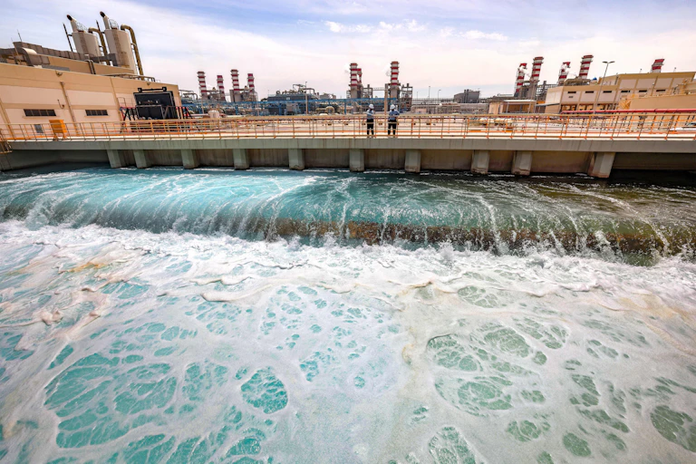 Two people stand on a large concrete platform overlooking a wide swath of flowing water.