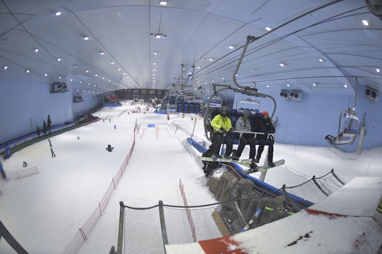 Under a massive roof, skiers slide down snow-covered slopes while others sit in a chairlift.