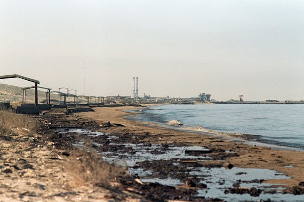 A beach with black oil on it and large buildings in the background.