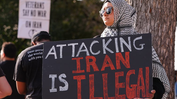 El respeto al derecho internacional depende de quién lo infringe: por qué Canadá apoyó la guerra contra Irán 1 Una mujer sostiene un cartel de protesta.