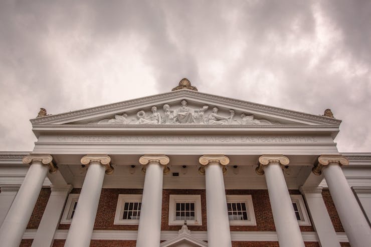 A university building with columns is seen against a gray sky.