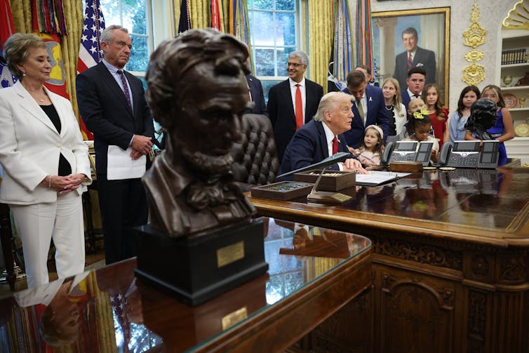 Trump ofreció un acuerdo restrictivo a las universidades que casi todas rechazaron, pero es posible que el Pacto sobre Excelencia Académica en la Educación Superior no esté del todo muerto. 1 Se ve a un grupo de personas de pie alrededor de un hombre de traje en una gran mesa de madera.