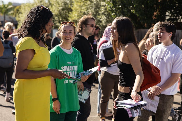 A woman in a yellow dress talks to people outside a polling booth
