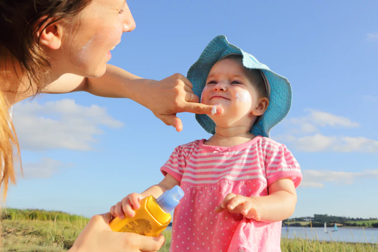 Woman applies sunscreen to the face of a young girl.