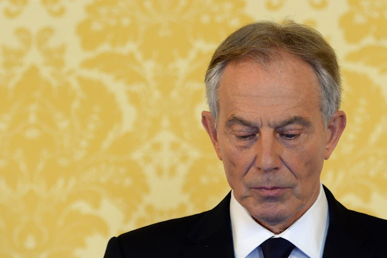 Blair looking somber in front of a wall of yellow wallpaper