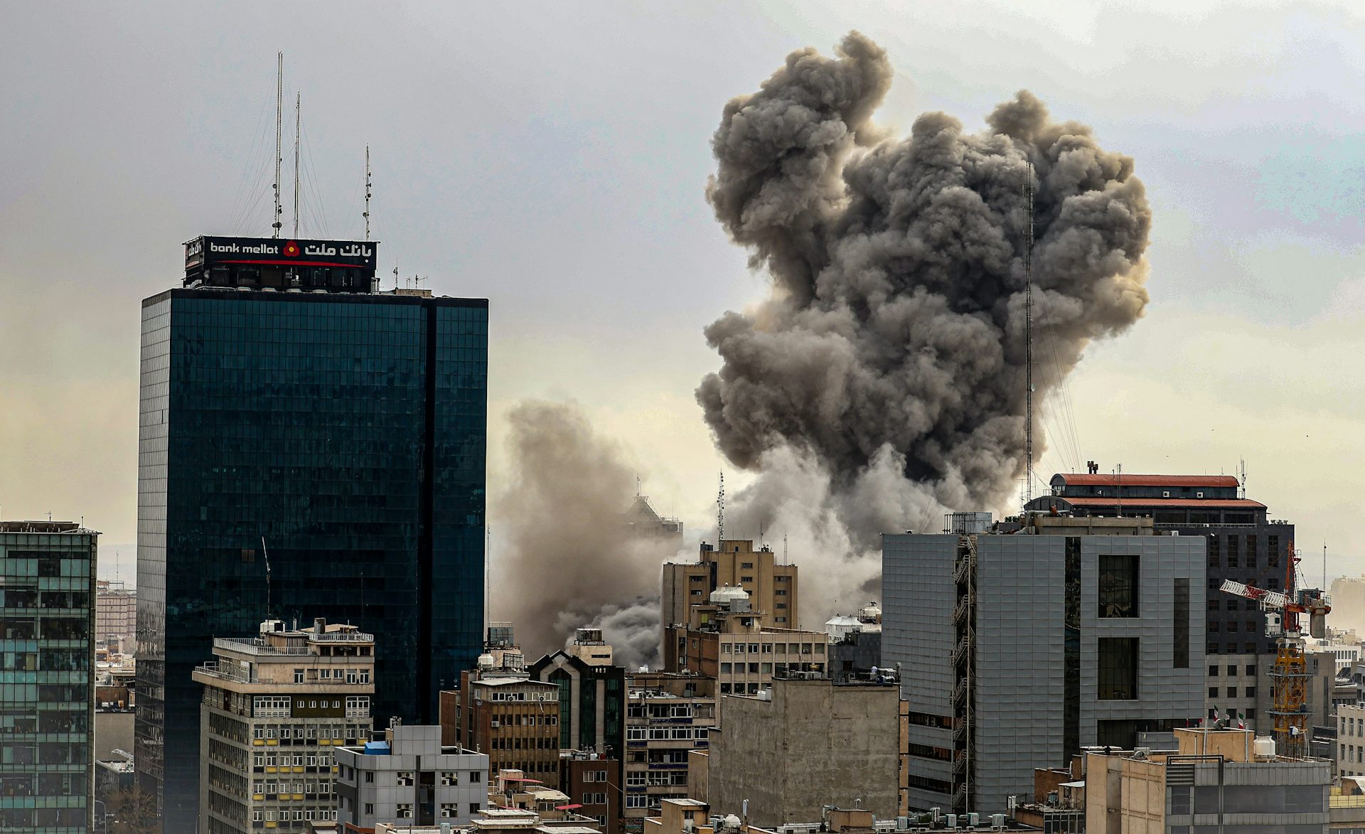 A dark plume of smoke rises above a city landscape