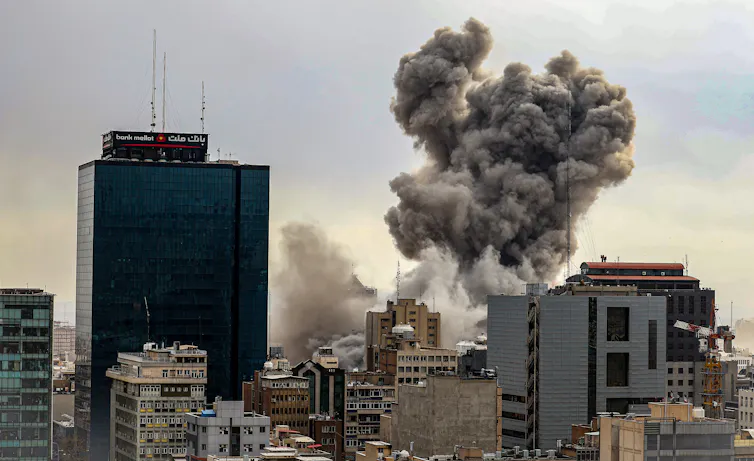 A dark plume of smoke rises above a city landscape