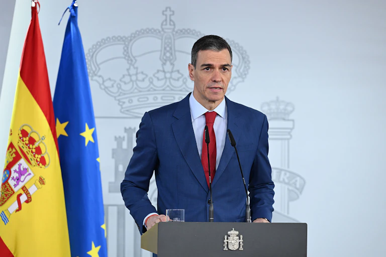 A man in a suit speaking behind a podium, with the flags of Spain and the European Union in the background