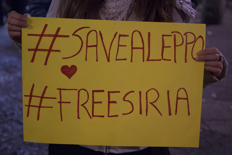 A protester holds a placard saying '#SaveAleppo' and '#FreeSyria'