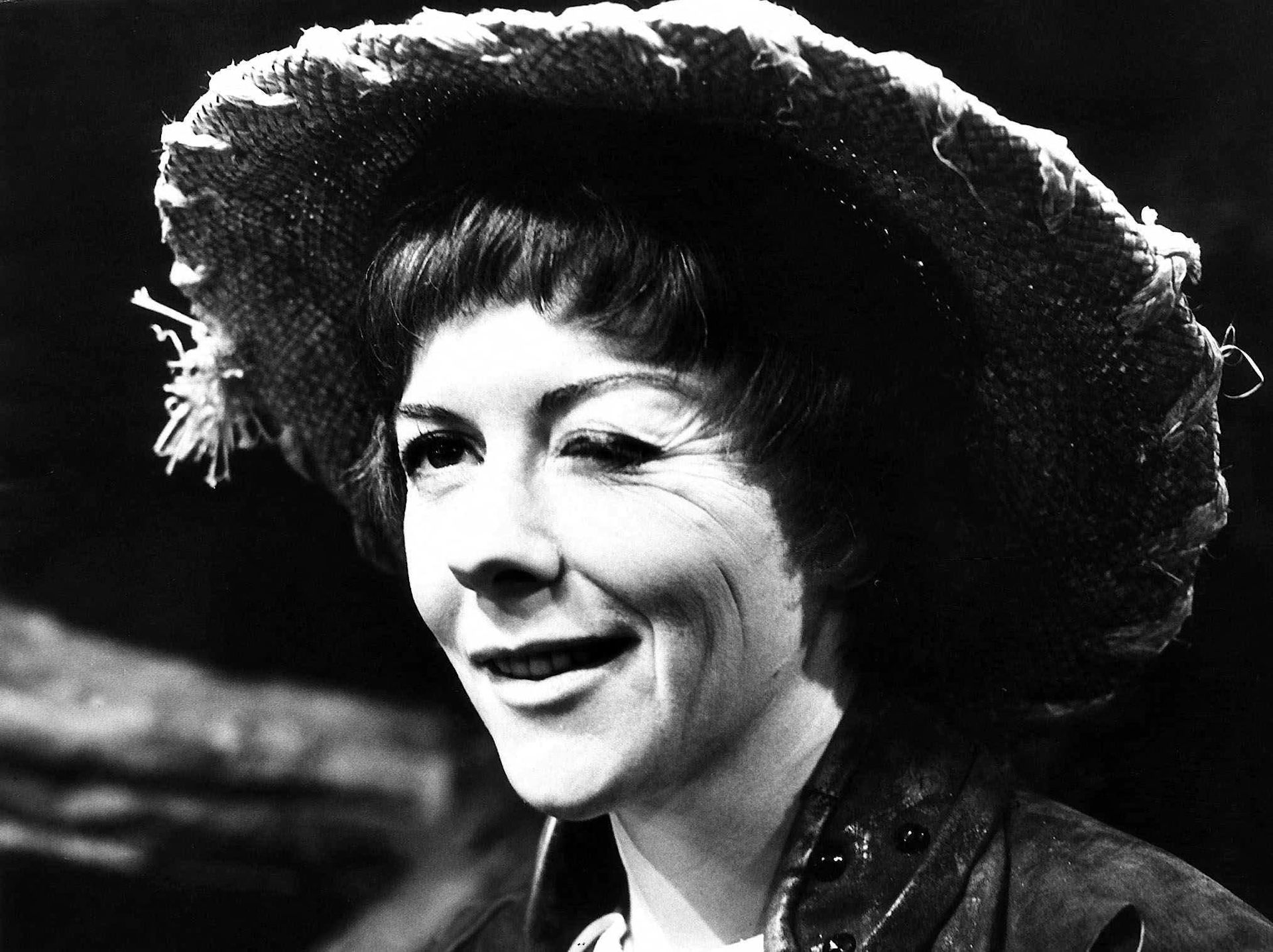 A black and white image of a woman in large hat winking at the camera.