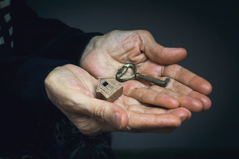 Close up of hands holding a key and a small model of a wooden bird house