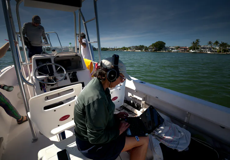 A woman on a boat wearing headphones and looking at a laptop