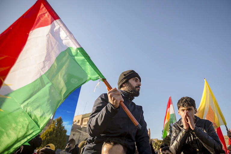 A man with a beard holds a green white and red flag.