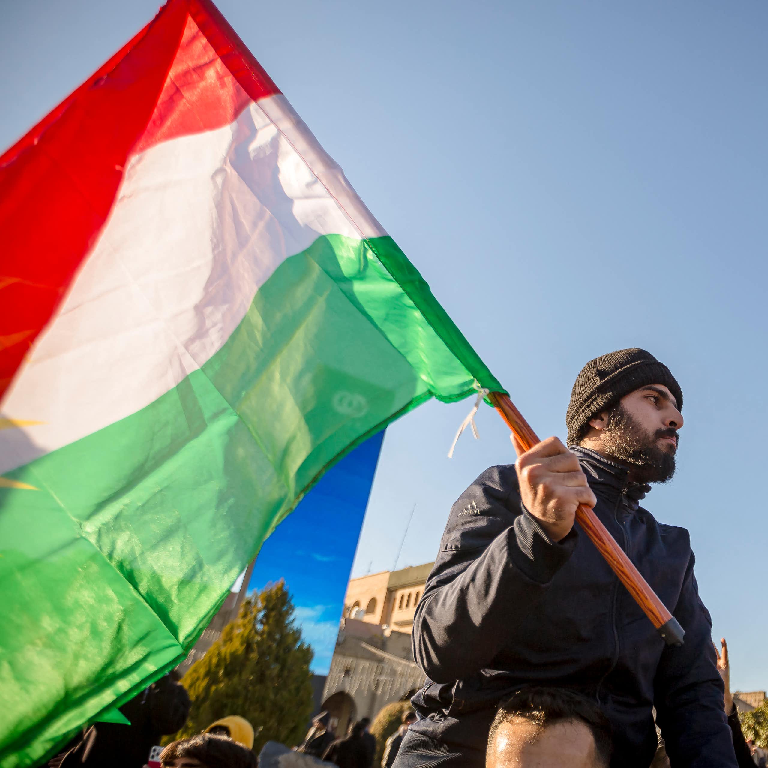 A man with a beard holds a green white and red flag.