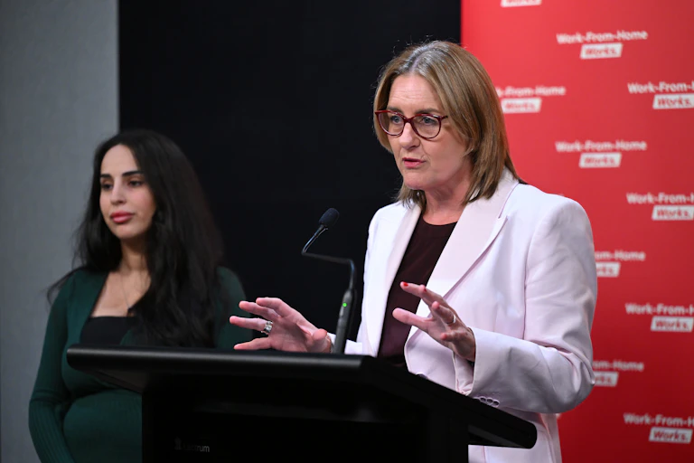 Jacinta Allan stands at a lectern on the right of the frame and speaks
