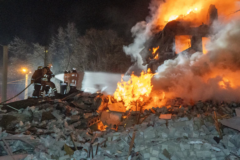 Firefighters with a hose on a flaming pile of rubble.