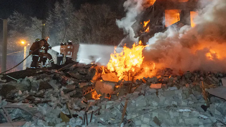 Firefighters with a hose on a flaming pile of rubble.