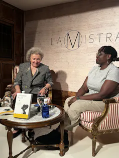 Dos mujeres, una blanca y una negra, se sientan detrás de una mesa baja mientras hablan en la presentación de un libro.