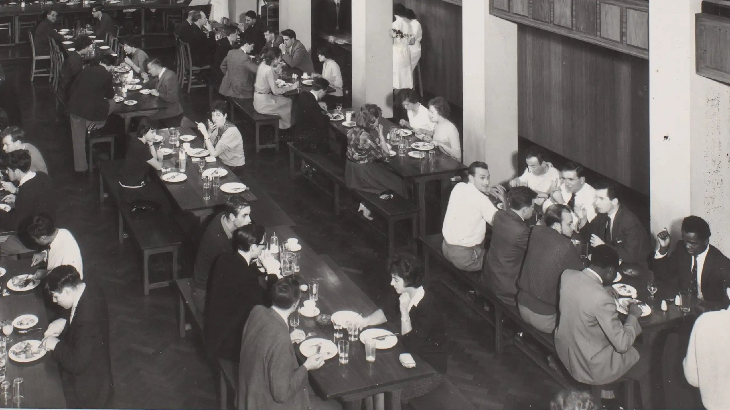 A black and white image of students eating a meal together in a university refectory in the 1960s