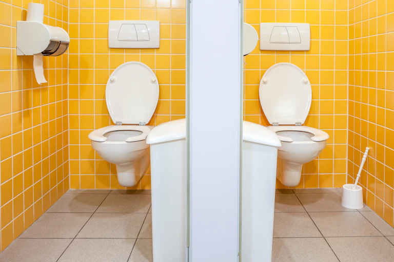 Two toilet cubicles with bright yellow tiled walls