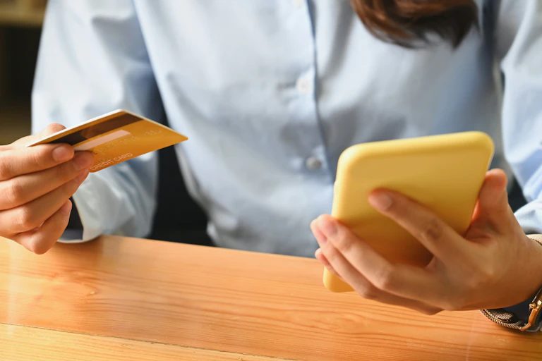A person holds a bank card while inspecting a cell phone.