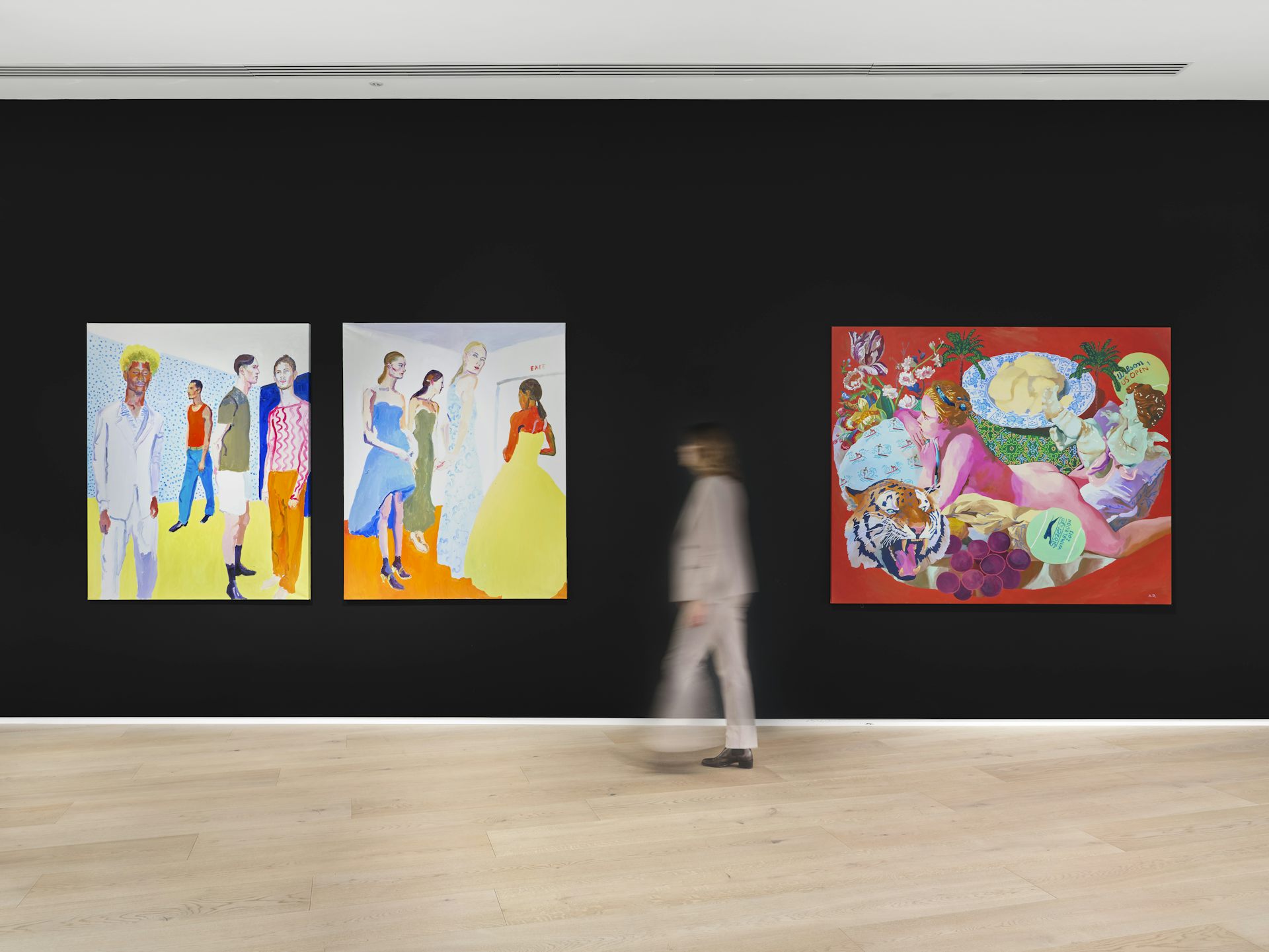 A person walking past very colourful paintings hung on a black wall