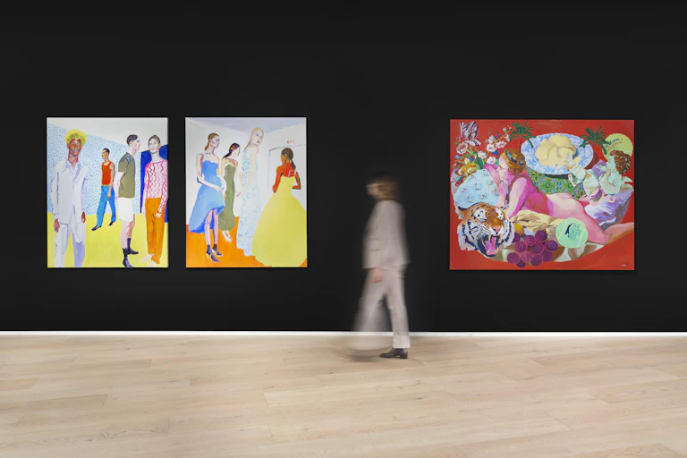 A person walking past very colourful paintings hung on a black wall
