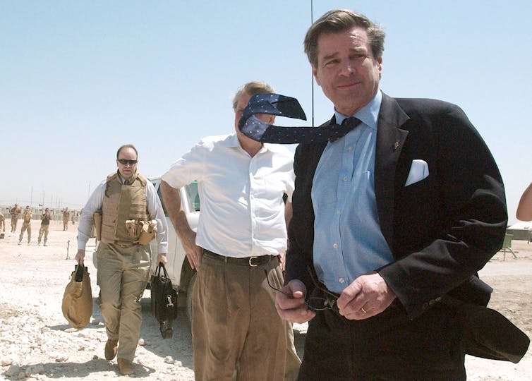 A man in a suit and tie walks in a desert.