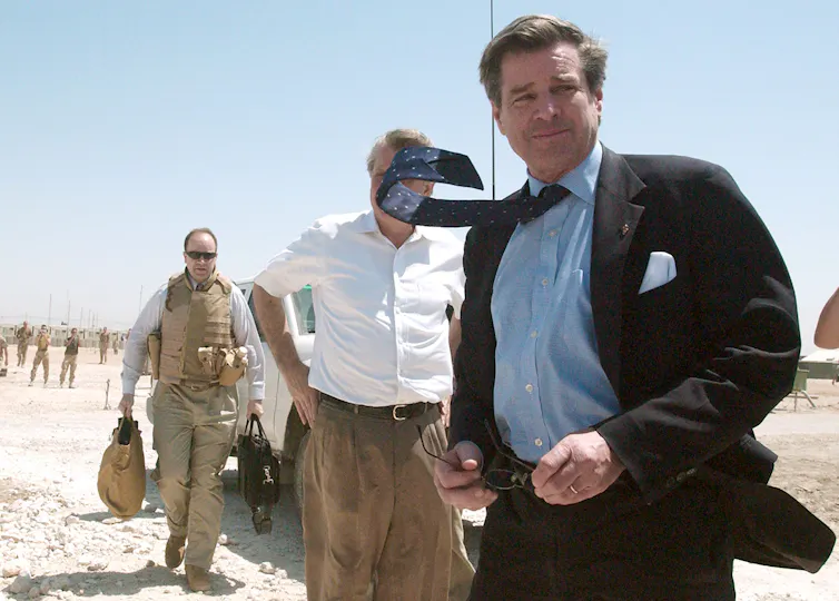 A man in a suit and tie walks in a desert.