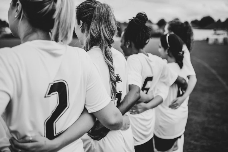 Black and white stock photo of women footballers of different races with their arms around each other