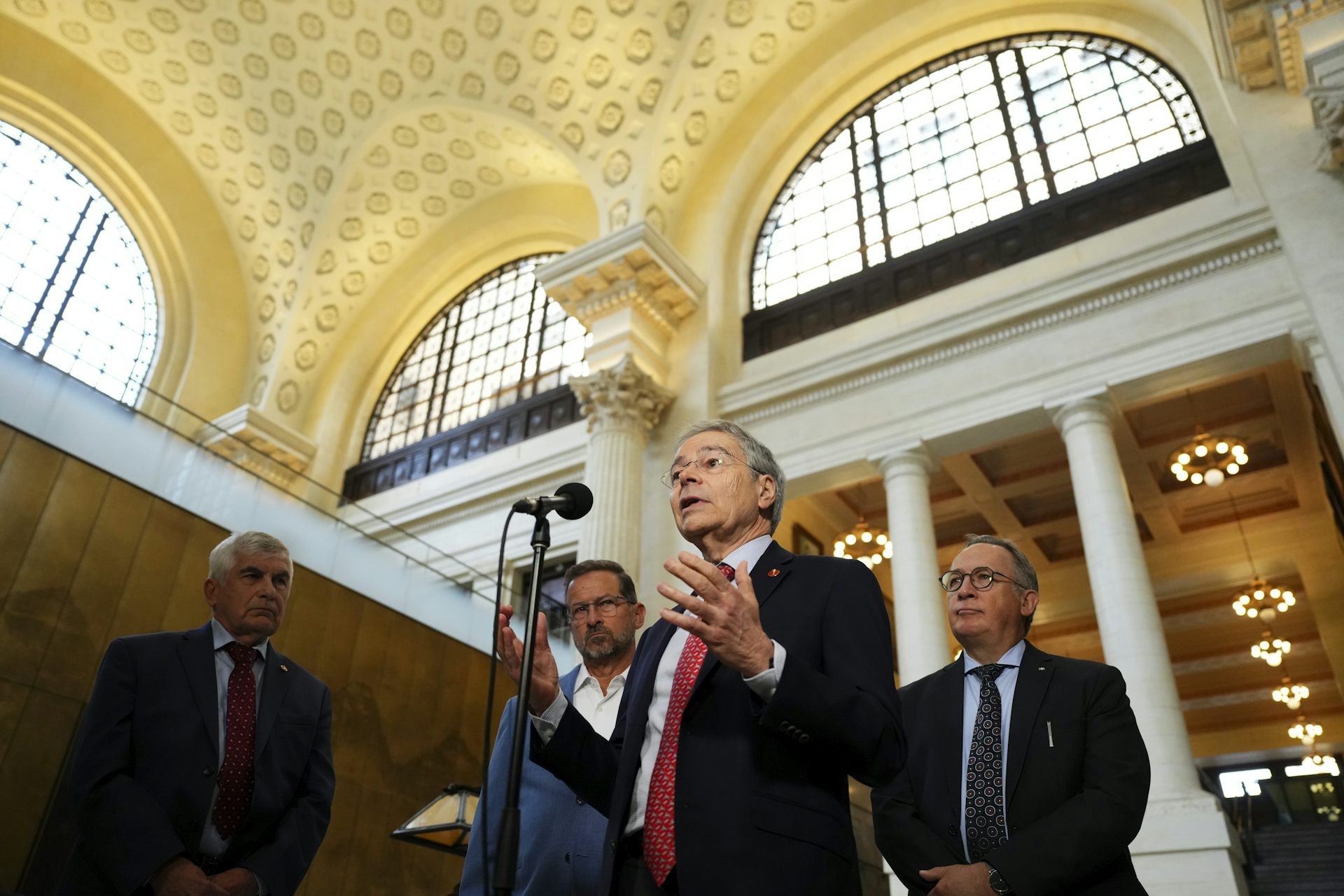 Un hombre de traje habla en un edificio ornamentado.