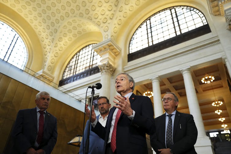 Un hombre de traje habla en un edificio ornamentado.