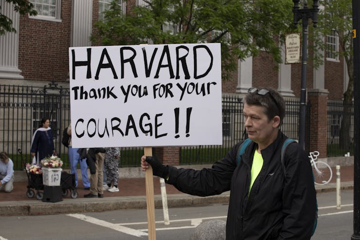 A man walks and holds a sign that says 'Harvard thank you for your courage!!'