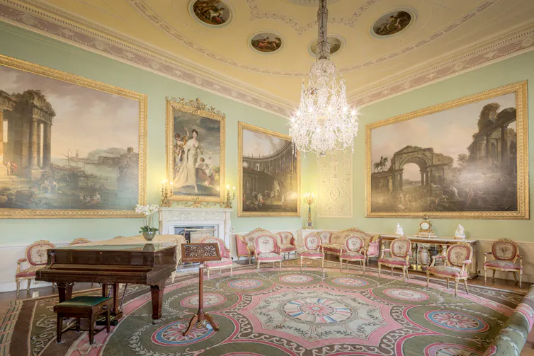 The music room at Harewood House has a piano, grand chandelier and ornate paintings on its walls.