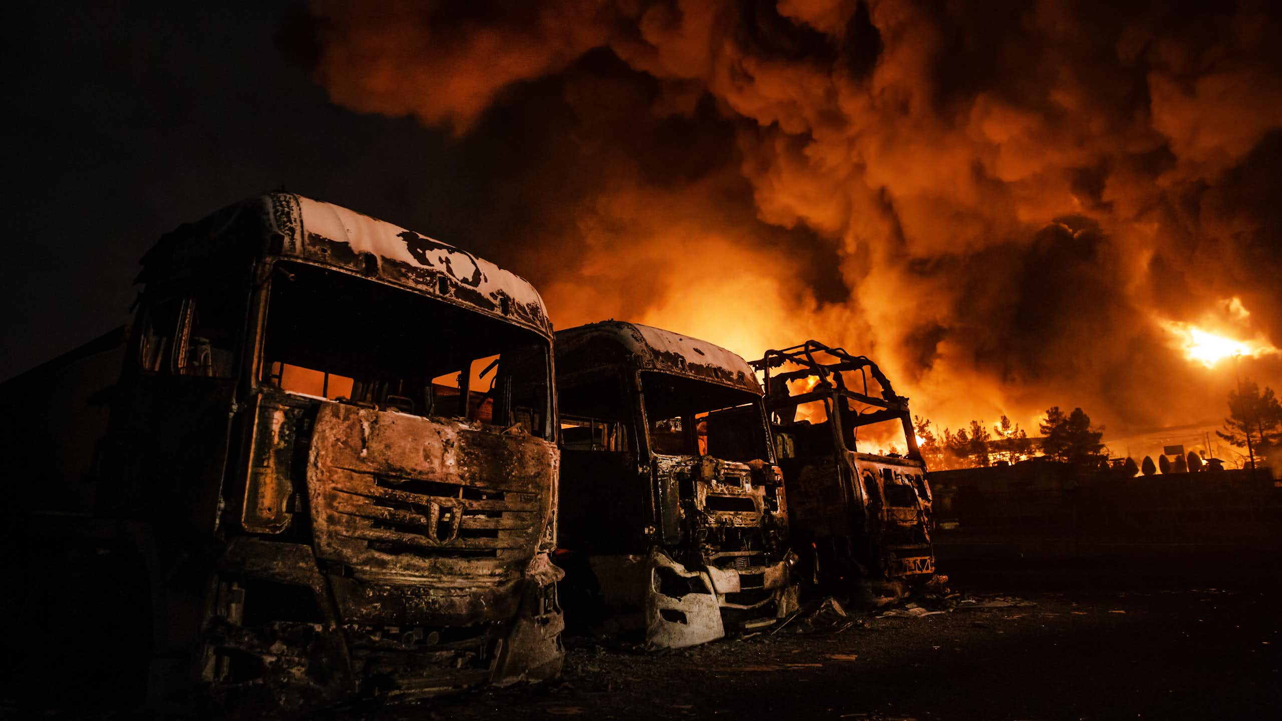 Fire rages behind burned-out buses.