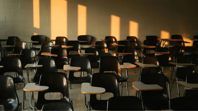 Chairs in an empty clssroom with long shadows cast on them by early or late day sun.