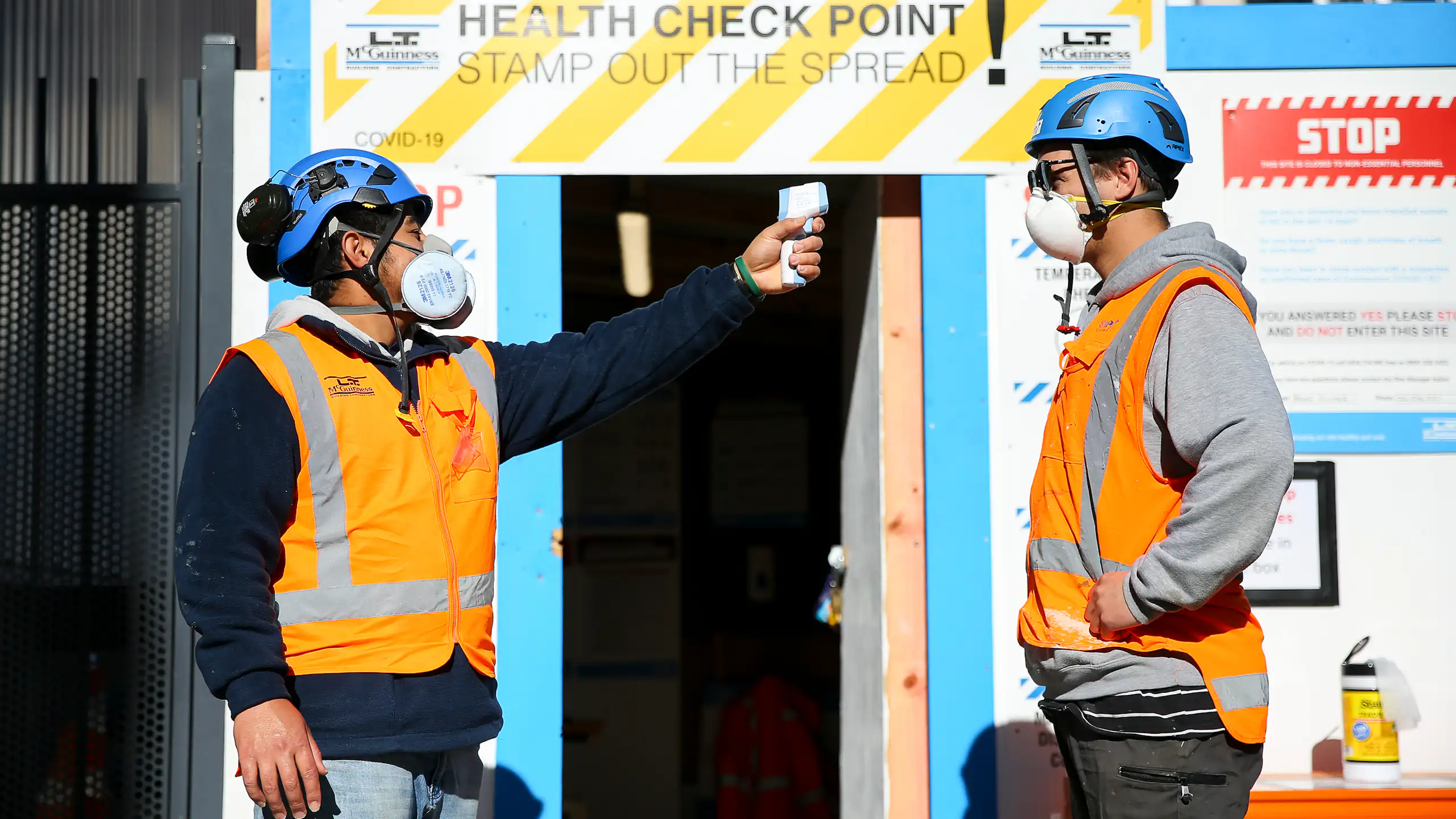 A worker conducts a temperature check at the entrance of a construction site during the COVID pandemic.