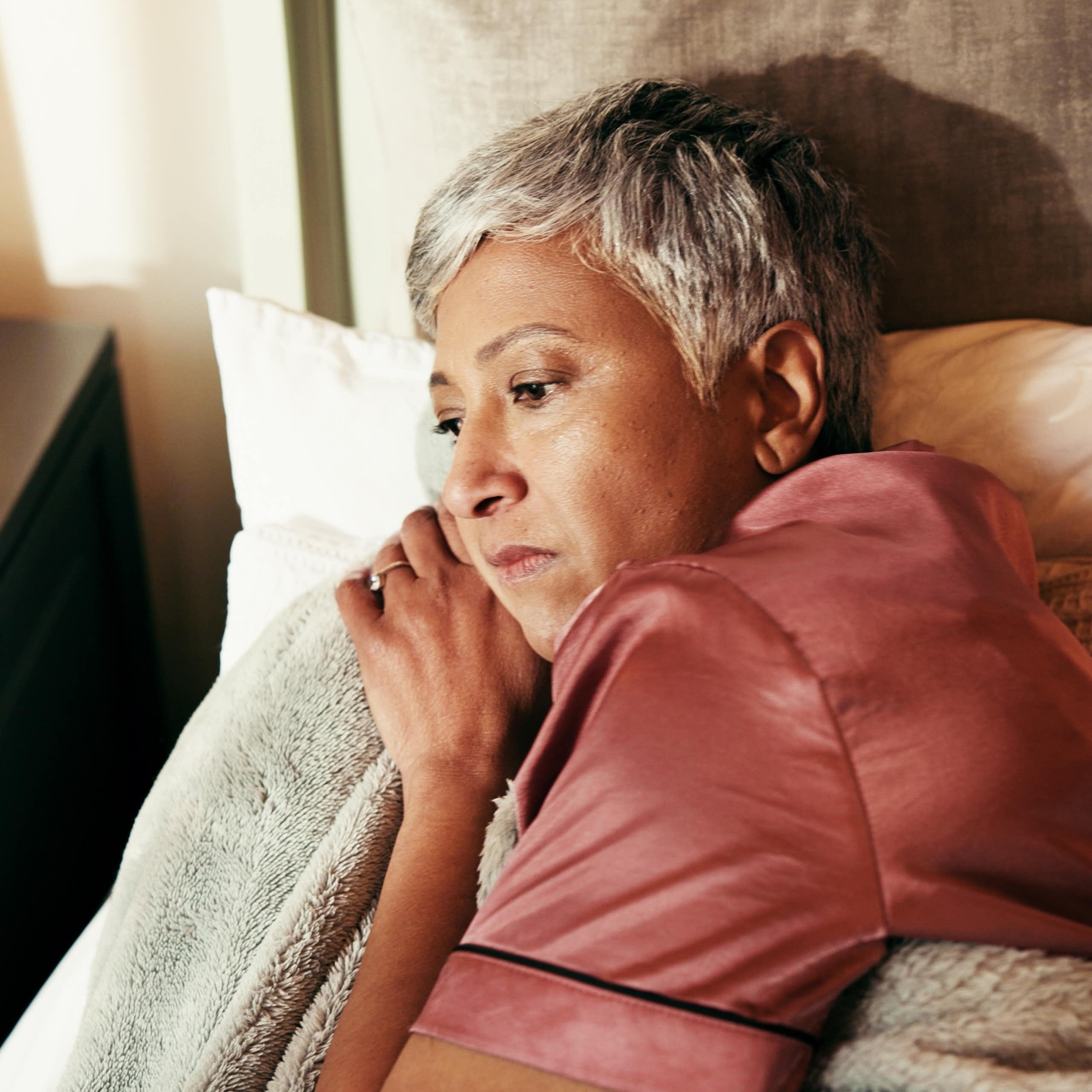 Une femme d’âge mûr est éveillée dans son lit, l’air préoccupé. Sur sa table de nuit se trouvent des boîtes de médicaments.