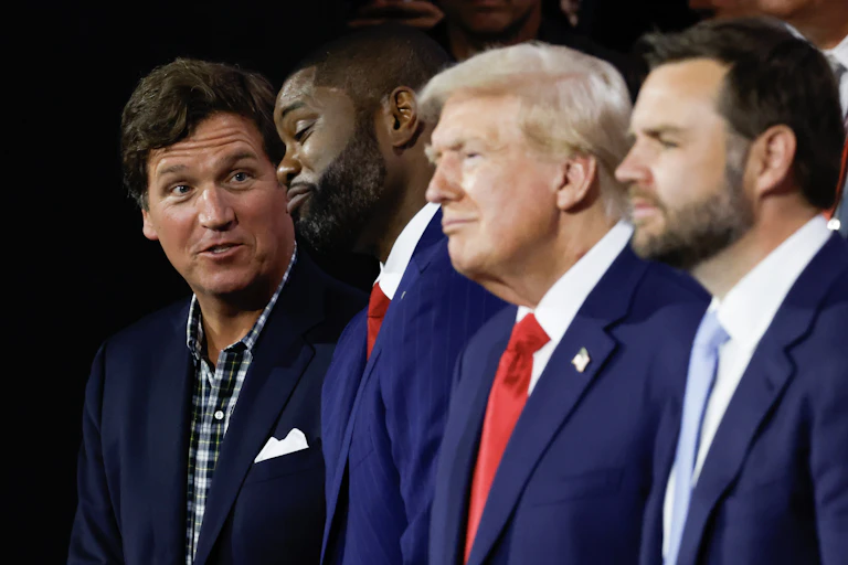 Tucker Carlson, in plaid shirt and suit jacket, with three men in suit and tie, including Donald Trump and JD Vance