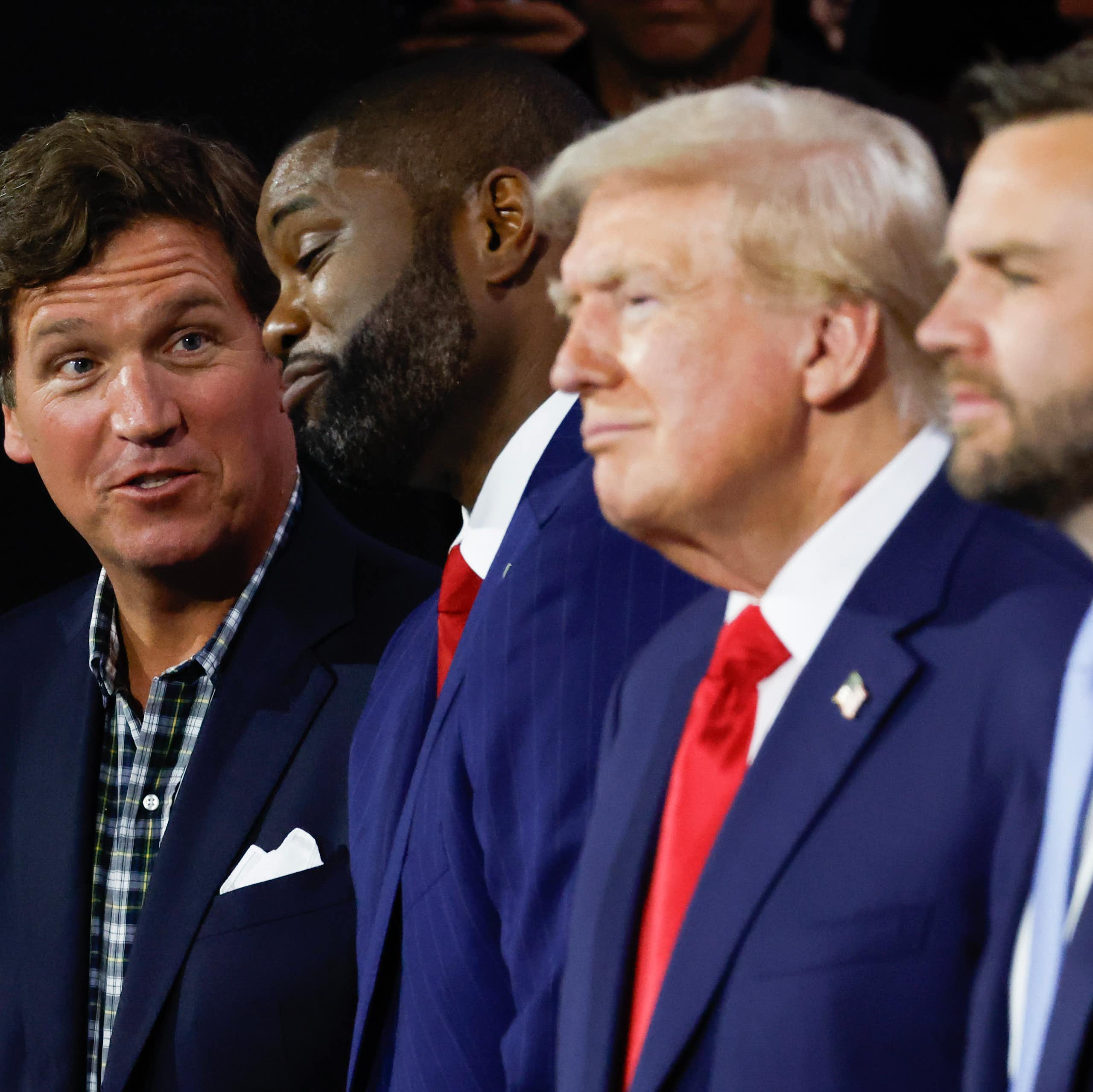 Tucker Carlson, in plaid shirt and suit jacket, with three men in suit and tie, including Donald Trump and JD Vance