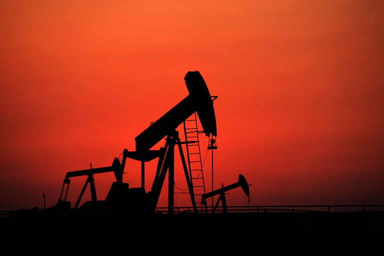 Oil pumps, which are large machines, working against a sunset.