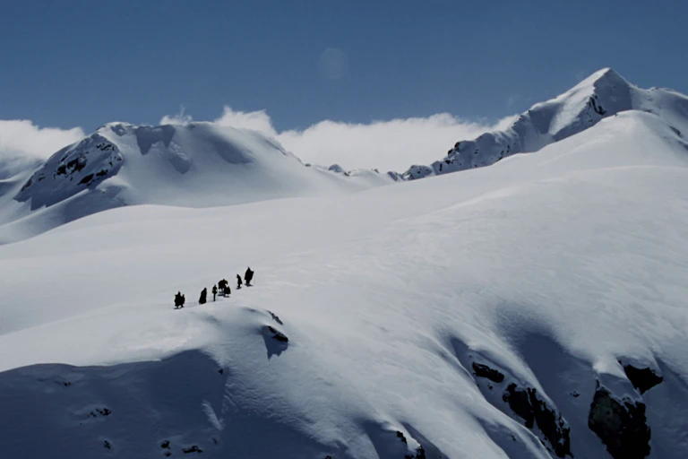 Tiny figures from a long distance crossing a snowy mountain pass.