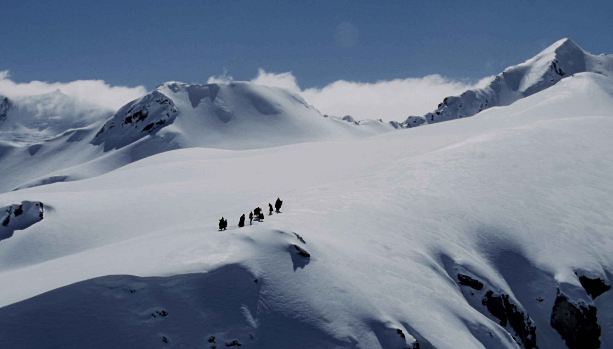 Tiny figures from a long distance crossing a snowy mountain pass.