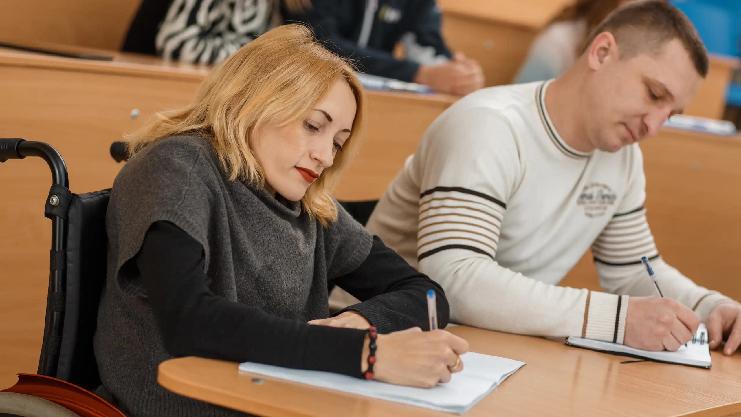 Disabled student with wheelchair taking notes in lecture theatre