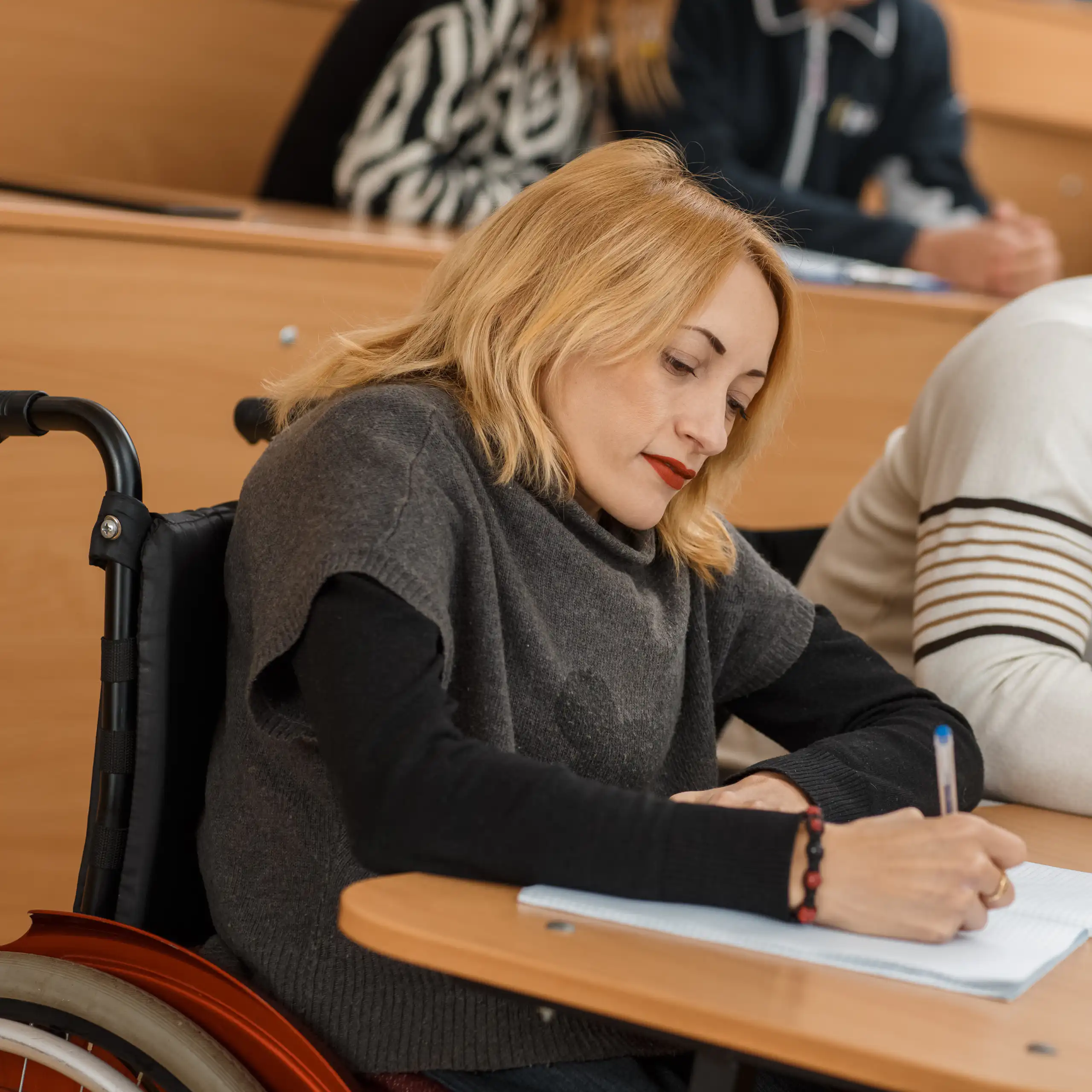 Disabled student with wheelchair taking notes in lecture theatre