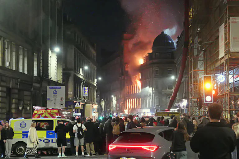 A city centre scene with fire raging in the distance and onlookers gathering with police.