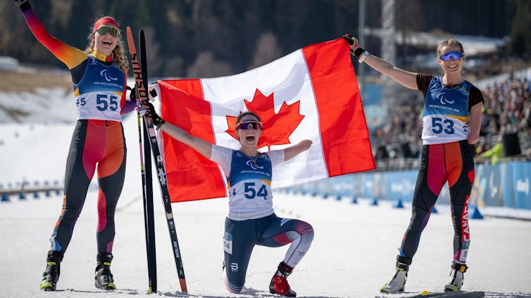 Tres atletas paralímpicos celebran la victoria y sostienen la bandera canadiense.