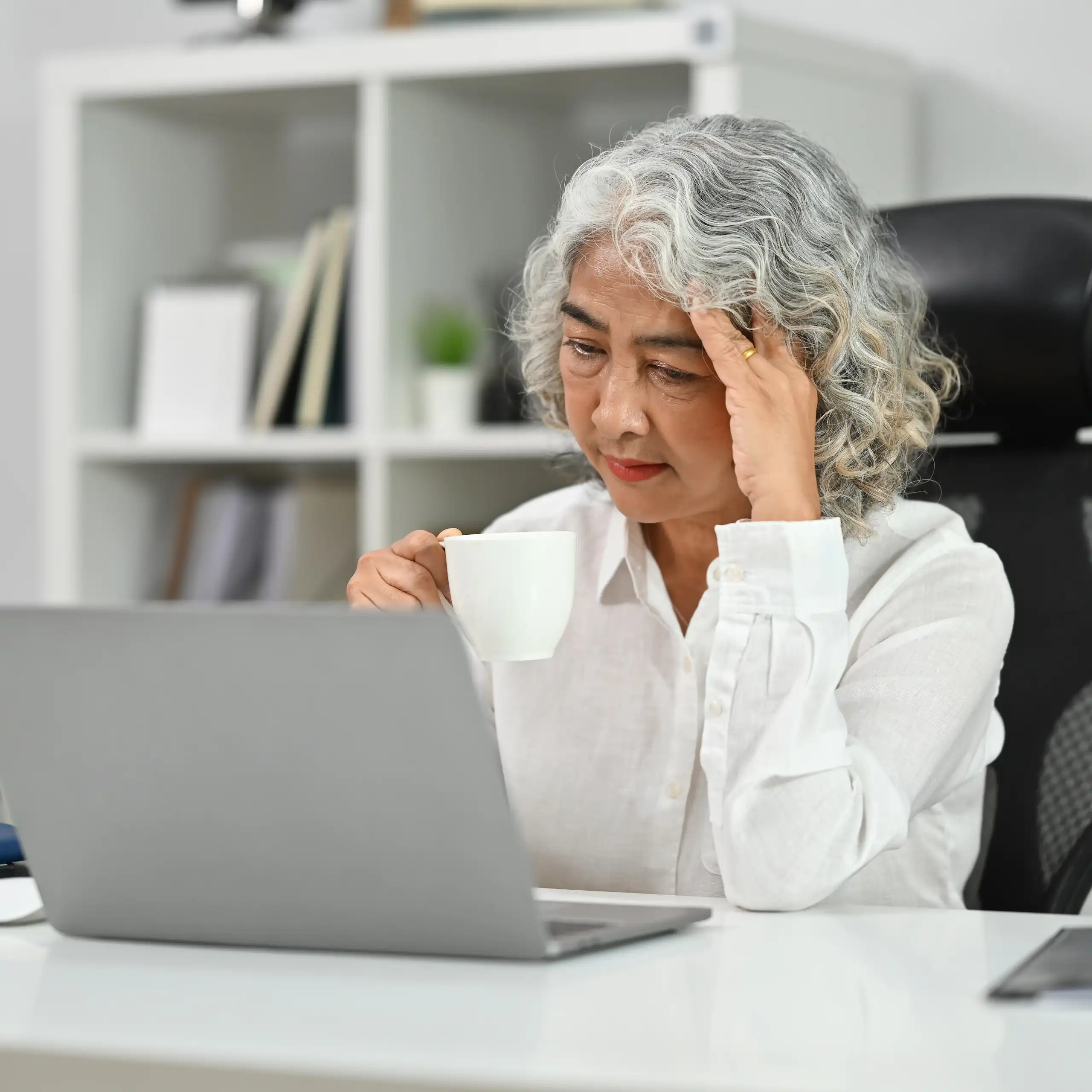 Une femme de plus de 50 ans travaille devant son ordinateur, en se tenant la tête avec une main.