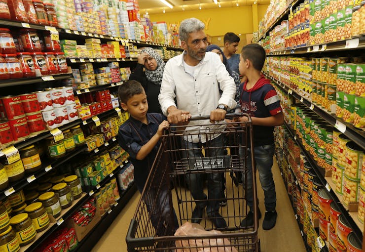 A man and his family push a cart through a supermarket.